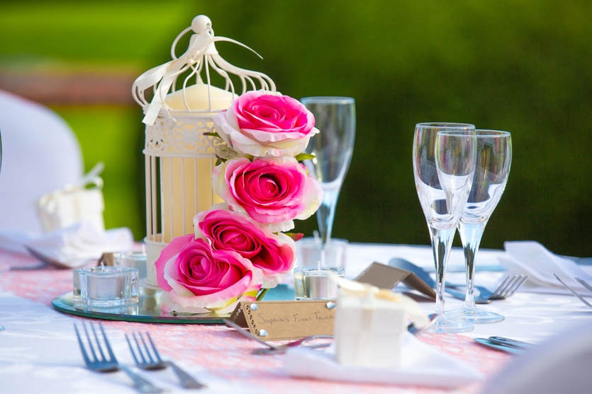 a table topped with a birdcage filled with pink roses.
