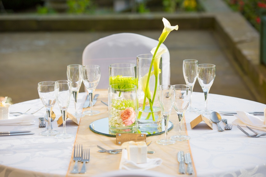 a table is set with glasses, silverware, and a vase with a flower.