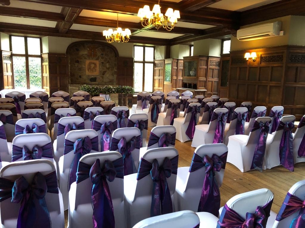 a room filled with lots of white chairs covered in purple sashes.
