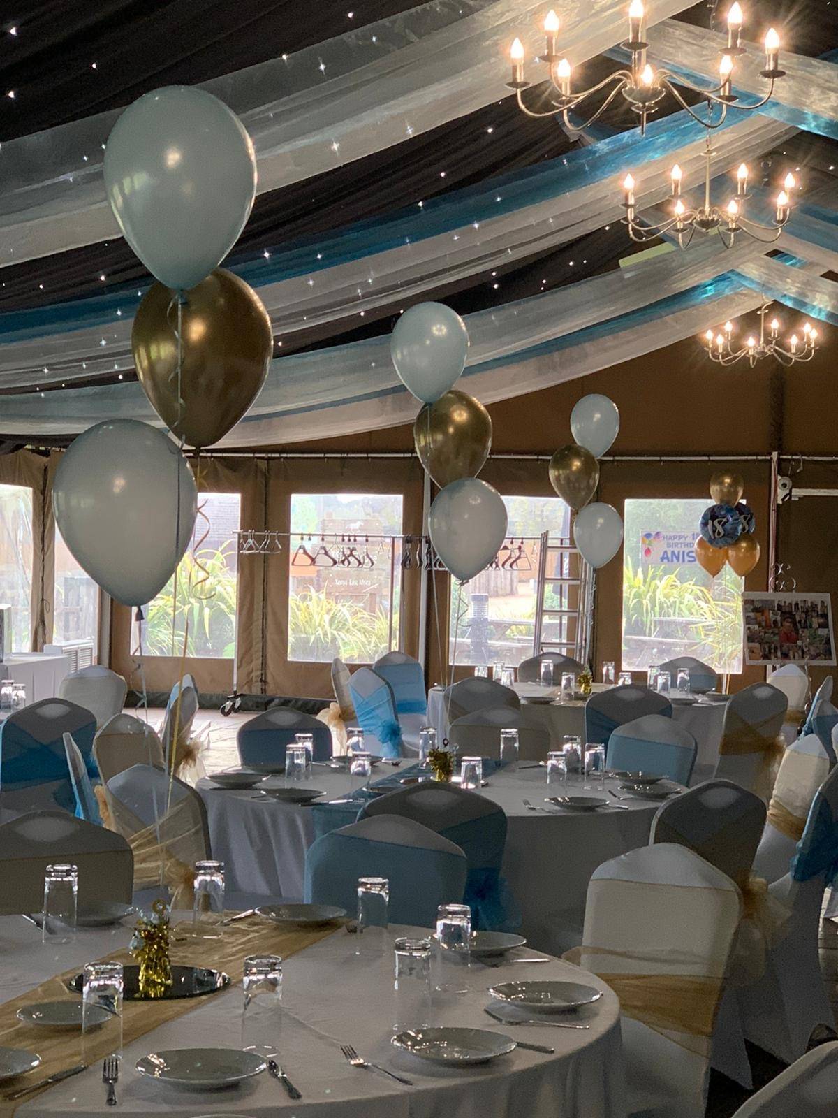 a room filled with lots of tables covered in white and gold balloons.