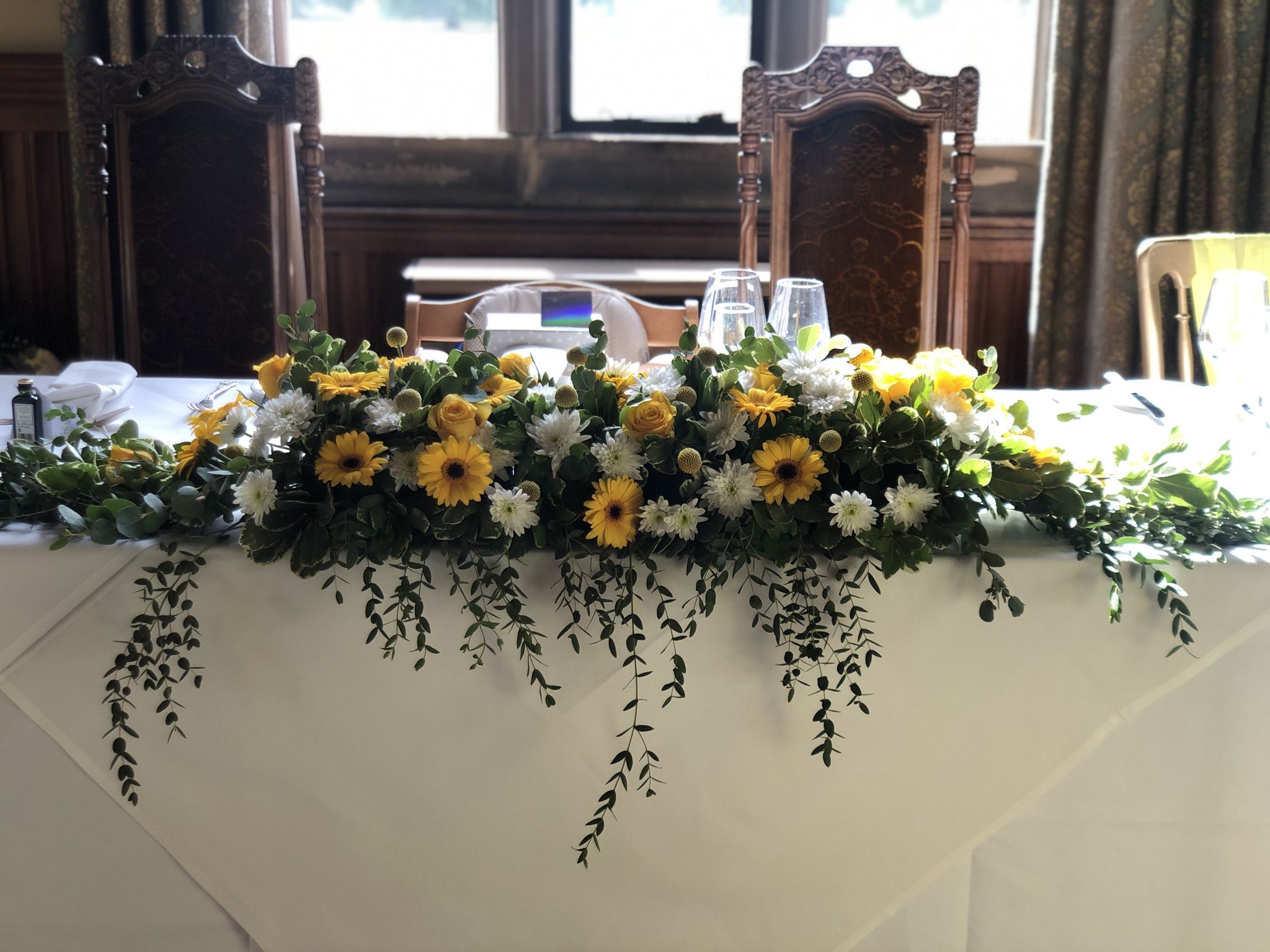 a table topped with a white table cloth covered in yellow and white flowers.
