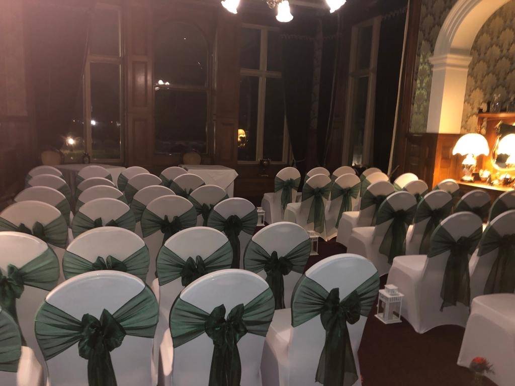 rows of white chairs with green sashes and bows.