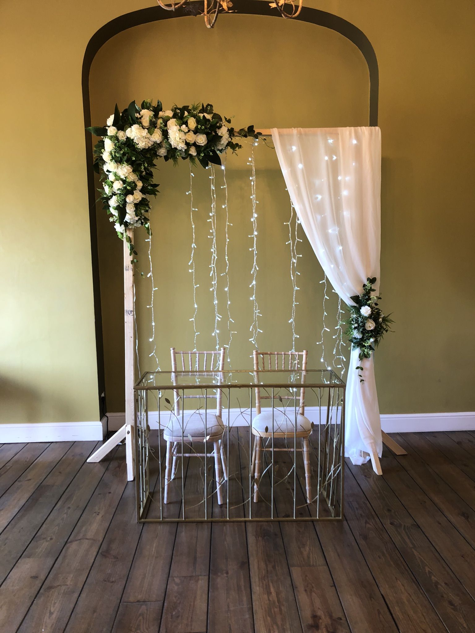 a wedding arch decorated with white flowers and greenery.