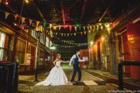 a bride and groom standing in an alley at night.