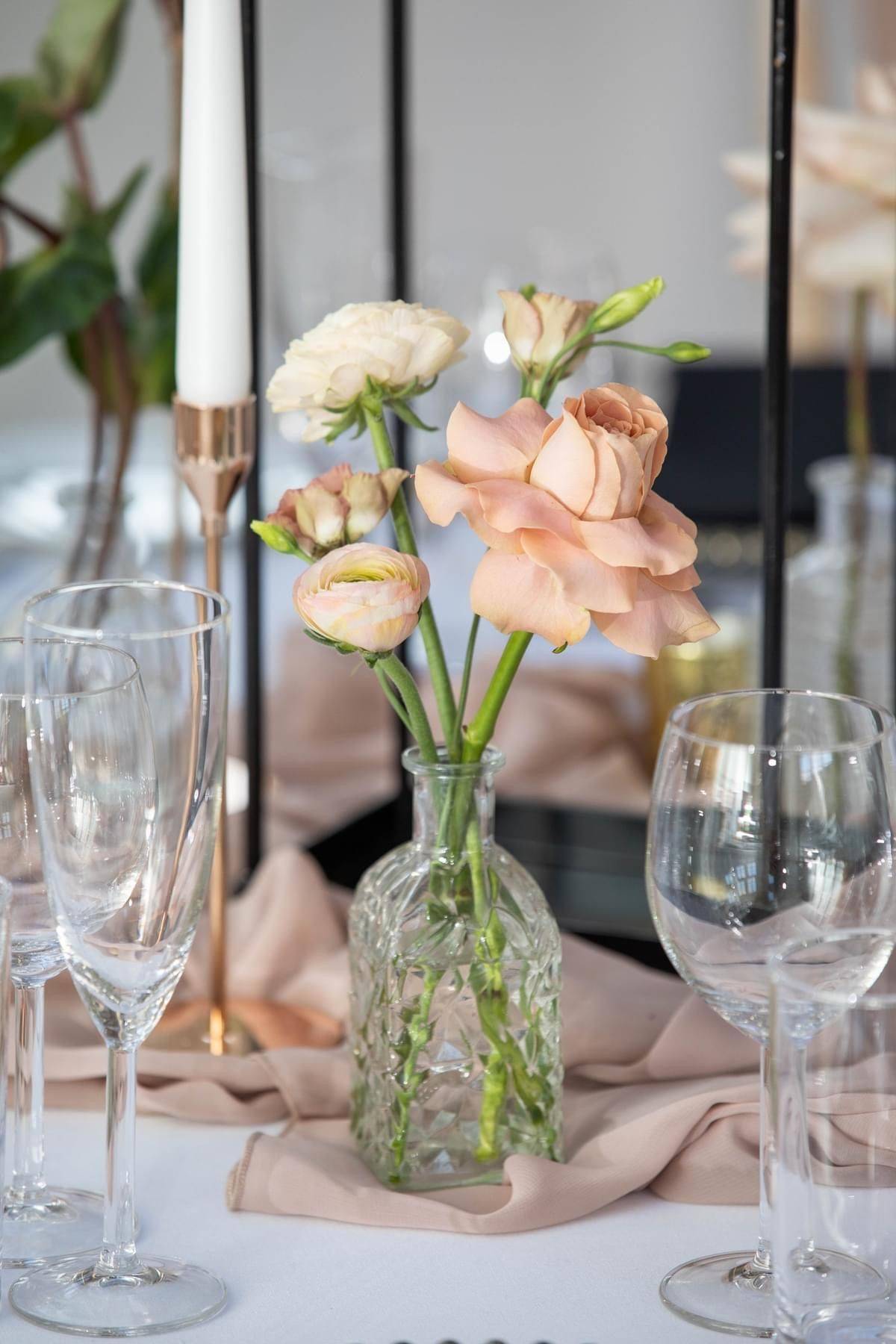 a vase of flowers on a table with wine glasses.