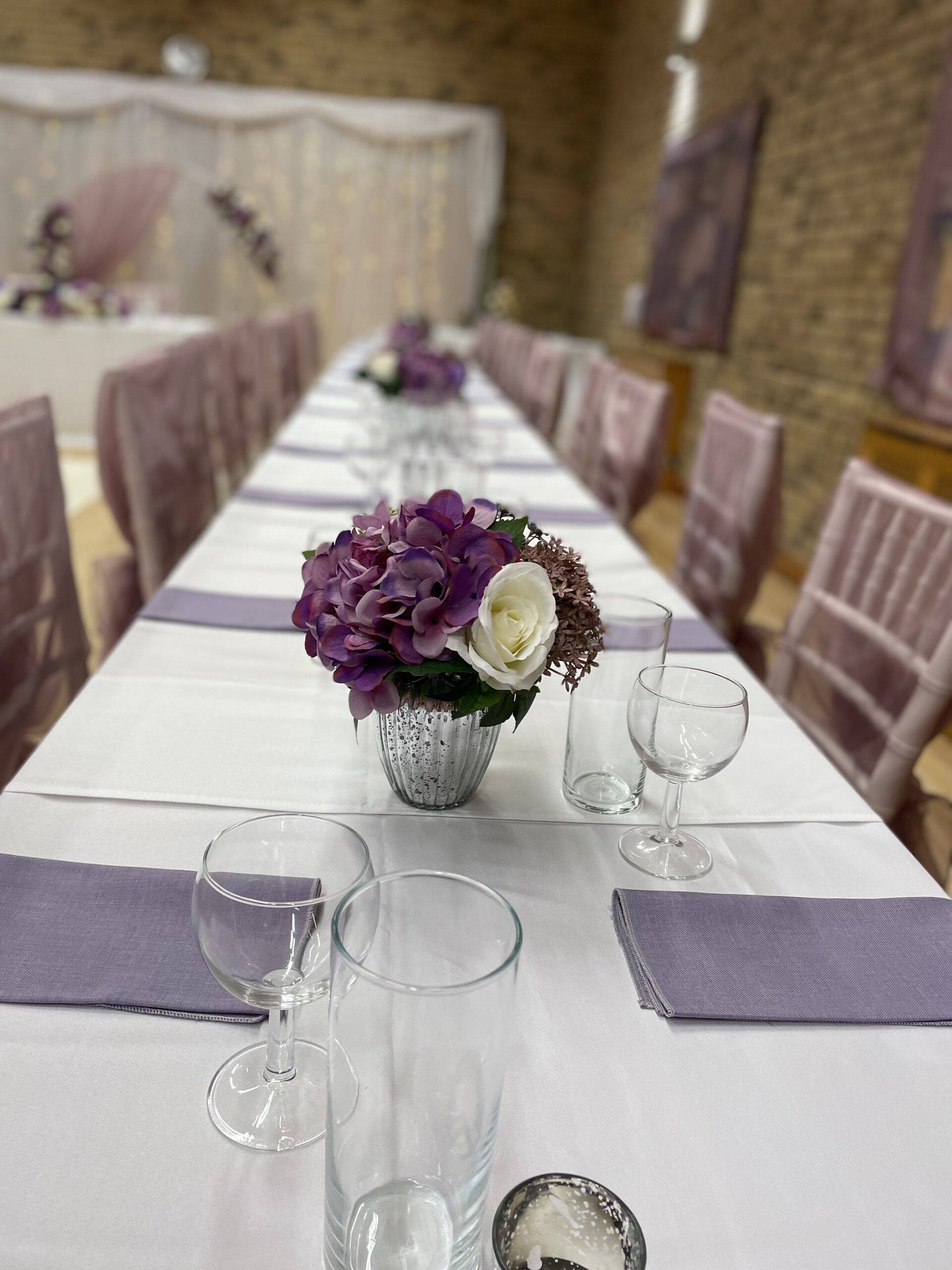 a long table with purple and white flowers in a vase.
